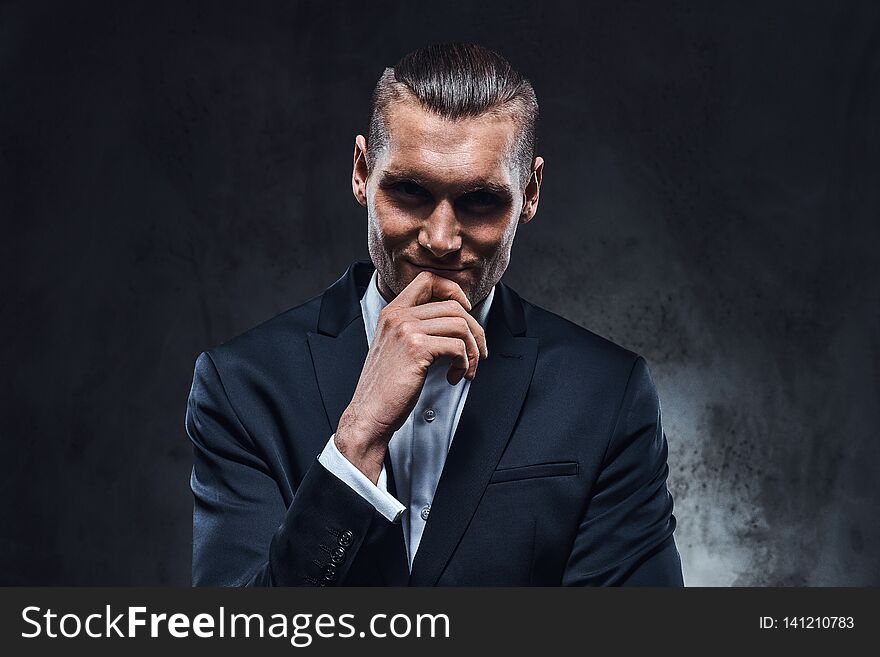 A confident businessman in black suit wearing elegant black suit. Studio shot on a dark textured wall