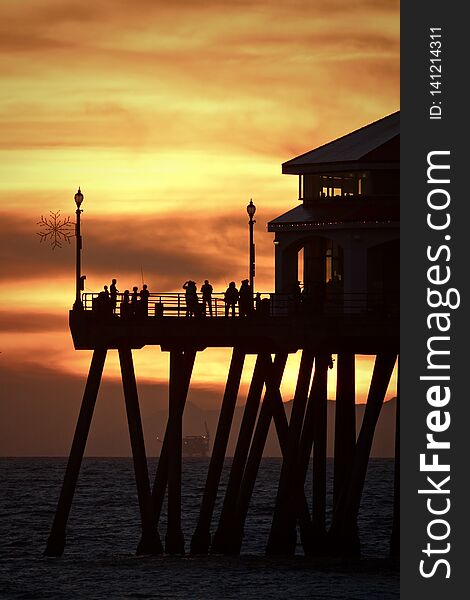 Silhouettes of people standing on the end of the Huntington Beach pier during a vibrant orange sunset over the ocean. Silhouettes of people standing on the end of the Huntington Beach pier during a vibrant orange sunset over the ocean