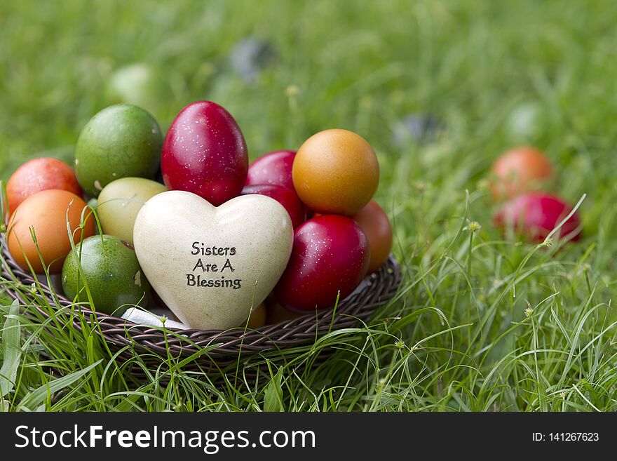 A basket of red, green orange and yellow Easter eggs sitting in a basket with sisters are a blessing ornament in the grass on a summer afternoon. A basket of red, green orange and yellow Easter eggs sitting in a basket with sisters are a blessing ornament in the grass on a summer afternoon