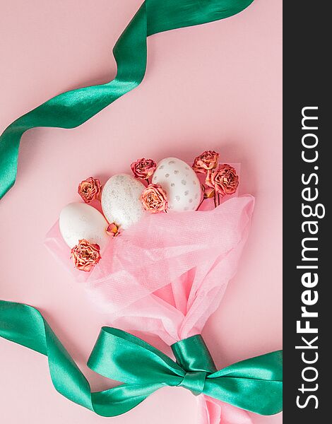 White Easter eggs in a bouquet with a green ribbon on pink background.