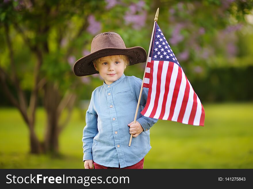 Cute toddler boy holding american flag in beautiful park. Independence Day concept
