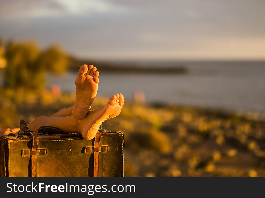 Travel concept image. beach and ocean in defocused backgorund and coulpe of female nude feet on old vintage luggage. resting after