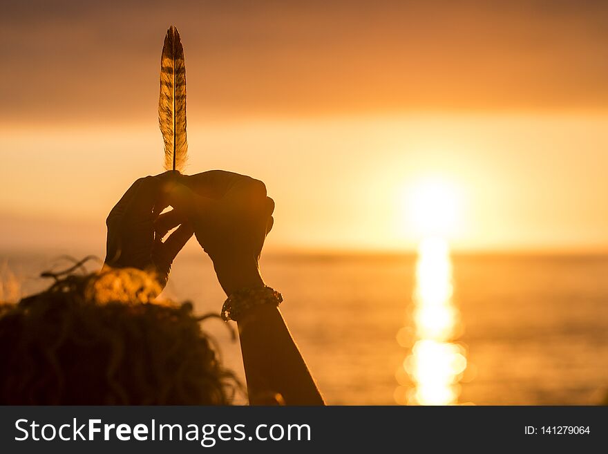 Woman hands taking a feather in front of an amazing golden and hot sunset over the sea. vacation and freedom independence concept. enjoying nature and feeling the world. conceptual image with weight and life