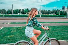 A Girl Rides A Bicycle In The Summer In The City On The Background Of Green Grass. Returns From A Bike Run In The Royalty Free Stock Photo