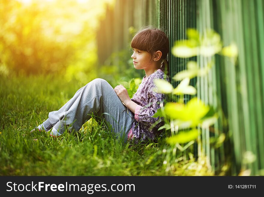 Little happy girl sitting on the grass in summer