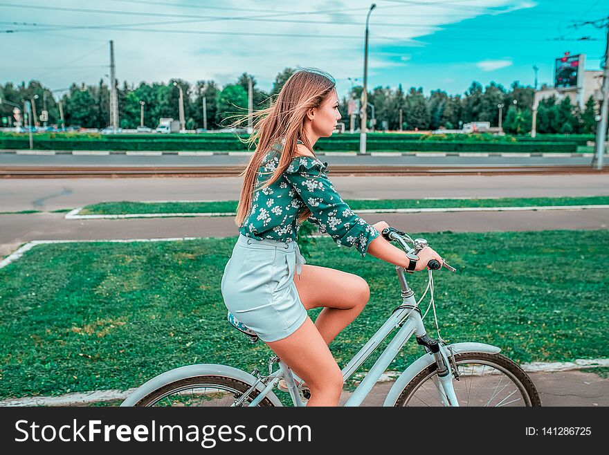 A girl rides a bicycle in the summer in the city on the background of green grass. Returns from a bike run in the