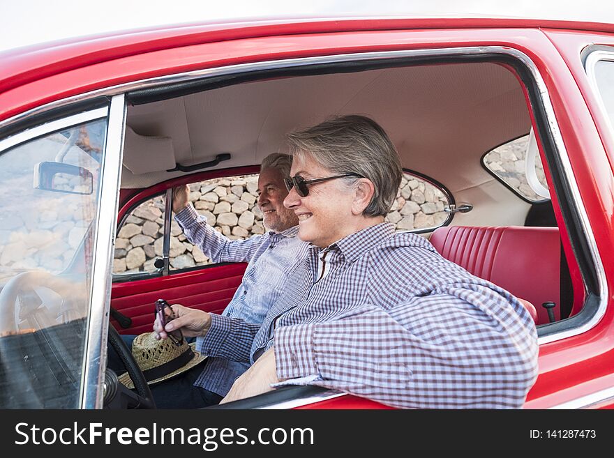 Nice adult couple hug and love inside a red old vintage car parked on the road. smiles and have fun traveling together. happiness
