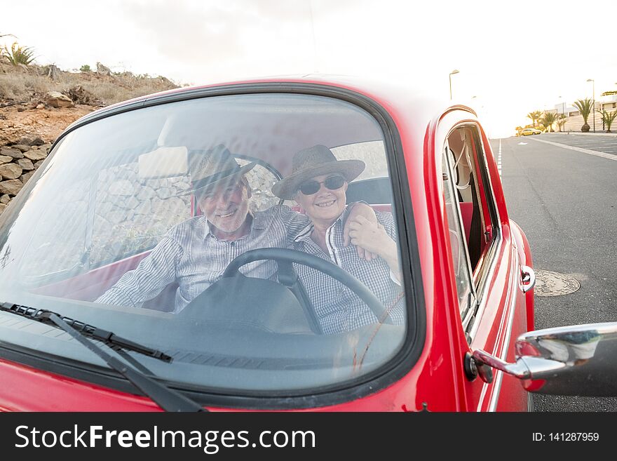 Nice adult couple hug and love inside a red old vintage car parked on the road. smiles and have fun traveling together. happiness