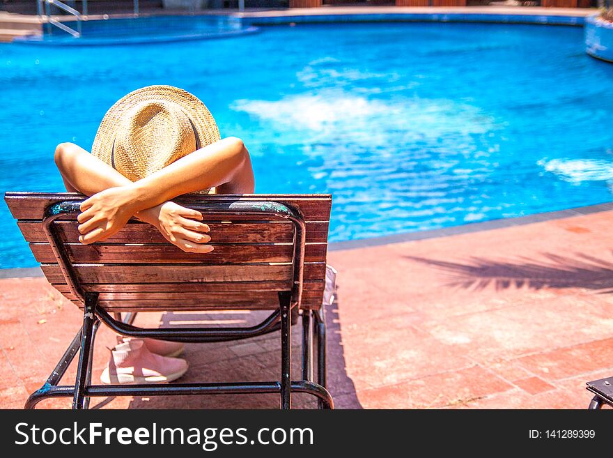Tourist in hat lies on louger near swimming pool for relax summer vacation concept.