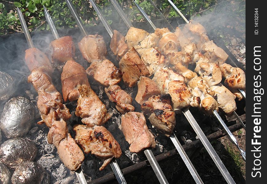 Delicious hot meat skewers on grill and baked potatoes in foil. Delicious hot meat skewers on grill and baked potatoes in foil