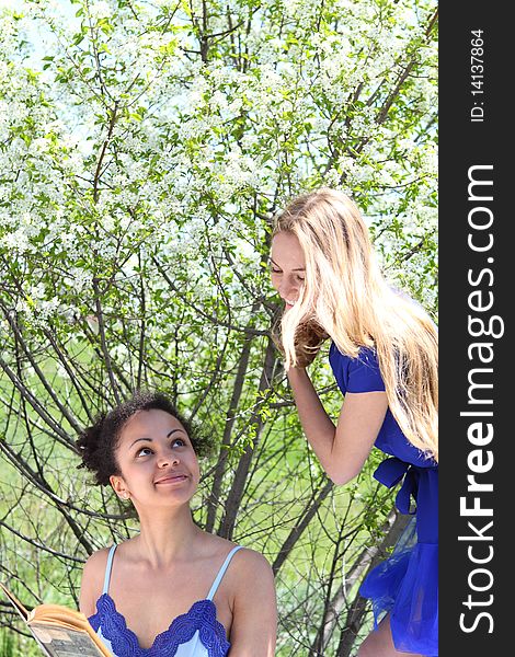 A beautiful mixed race African American girl and Caucasian blonde girl reading in the garden. A beautiful mixed race African American girl and Caucasian blonde girl reading in the garden