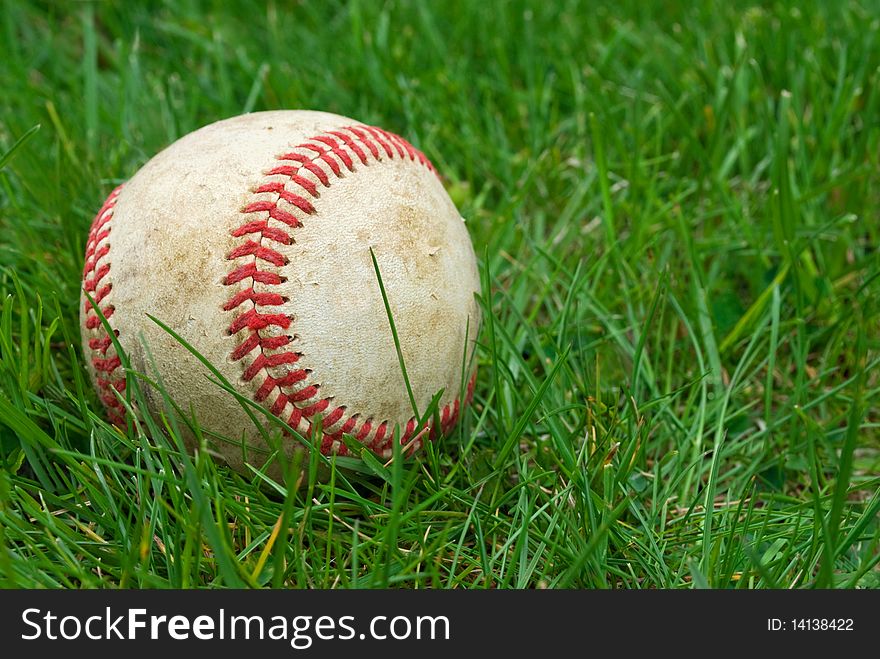 Closeup of baseball in the grass, shallow depth of field with focus on ball, copy space at right. Closeup of baseball in the grass, shallow depth of field with focus on ball, copy space at right