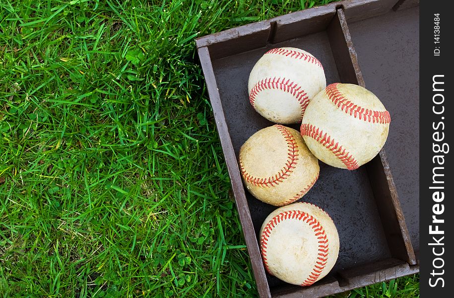 Collection of old baseballs in a wooden box, copy space on grass at left. Collection of old baseballs in a wooden box, copy space on grass at left