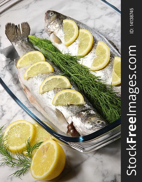 Fish on a white plate with lemons and dill on stone