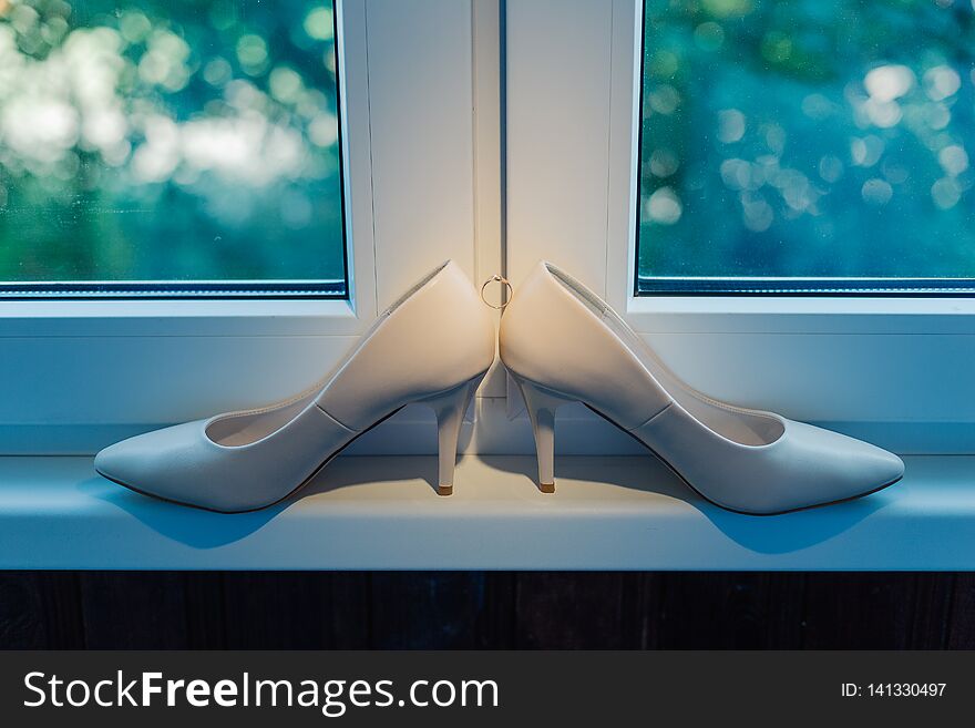 Women`s beautiful wedding shoes on the window with a wedding ring.