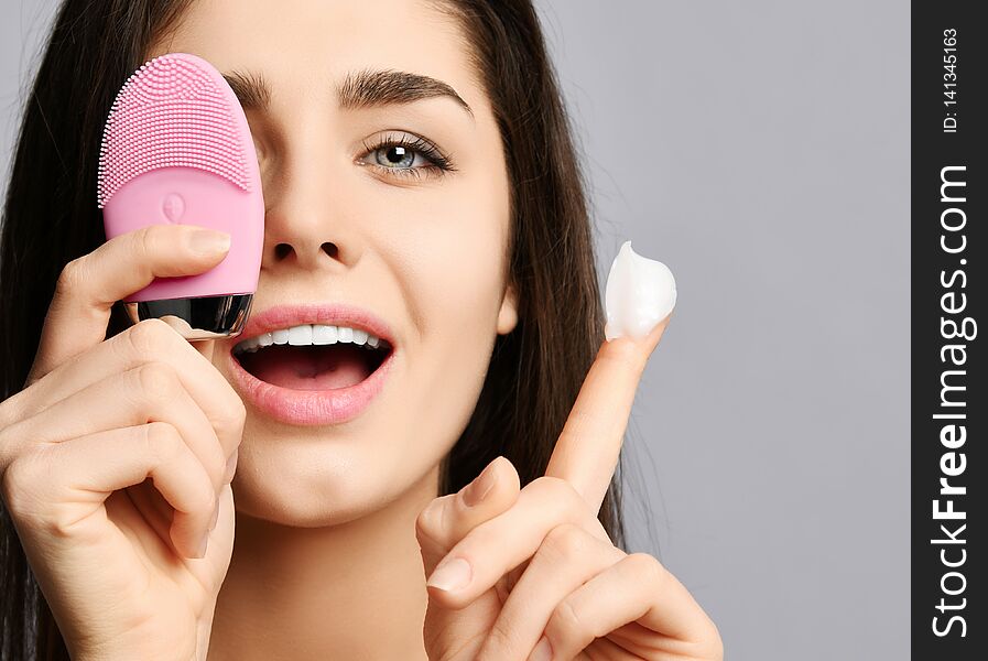 Beautiful woman hold pink face exfoliator brush silicone cleansing device for sensitive normal skin and cream