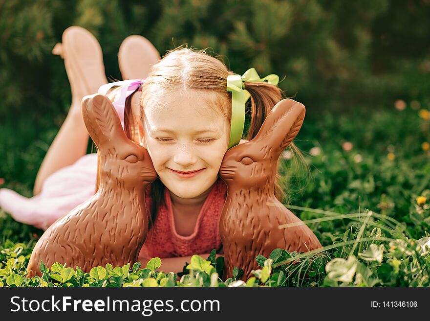 Outdoor portrait of a cute little girl playing in a garden with two chocolate bunnies. Outdoor portrait of a cute little girl playing in a garden with two chocolate bunnies