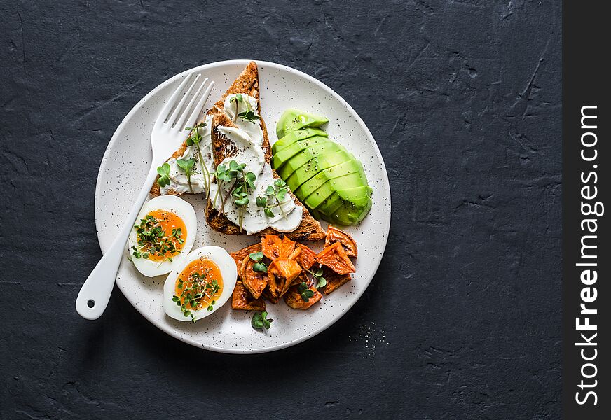 Cream cheese toast, avocado, boiled egg, baked sweet potatoes - delicious healthy breakfast or snack on a dark background