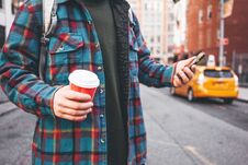 Casual Young Man Walking On City Street Hold Cup Of Hot Coffee In Hand And Using Mobile Phone For Video Link Royalty Free Stock Photos