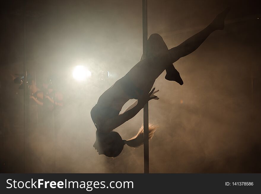 Young Woman Exercise Pole Dance On A Dark Background.