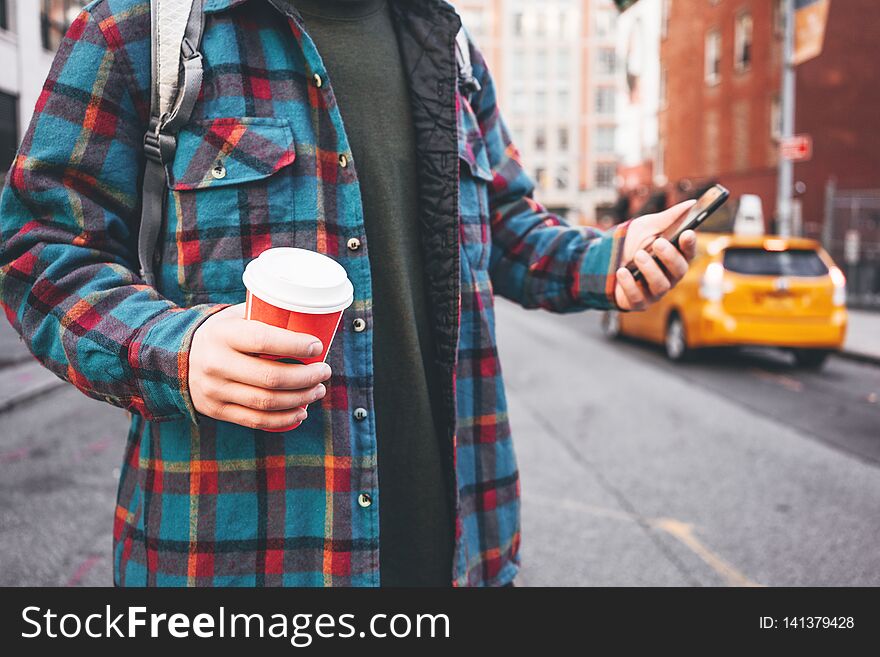 Casual Young Man Walking On City Street Hold Cup Of Hot Coffee In Hand And Using Mobile Phone For Video Link