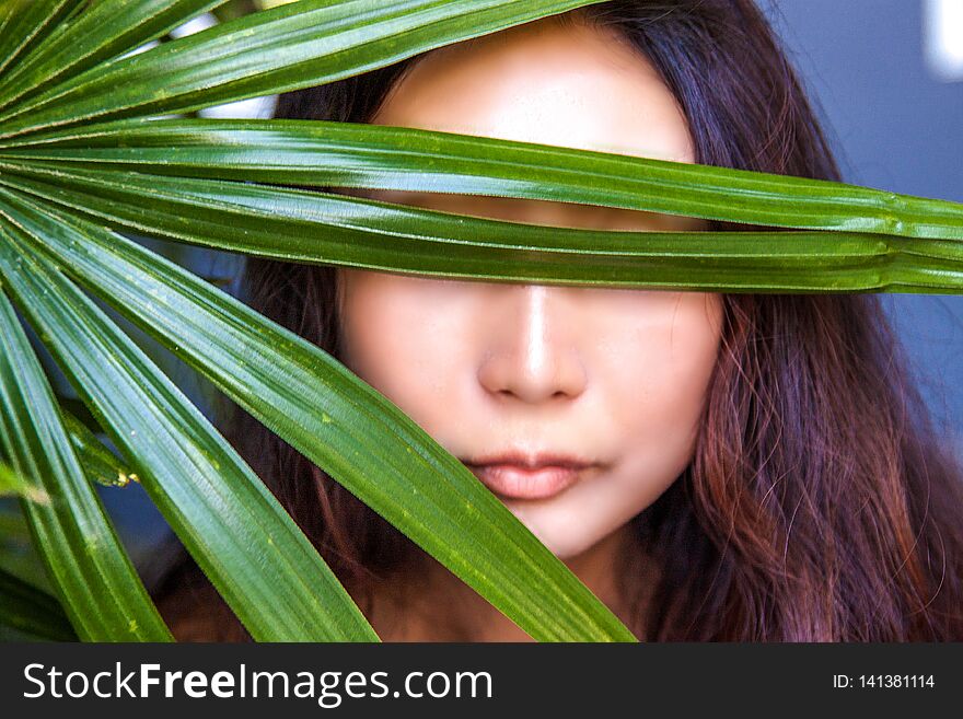 A beautiful woman is hiding behind palm leaves. Eastern beauty and skin care.