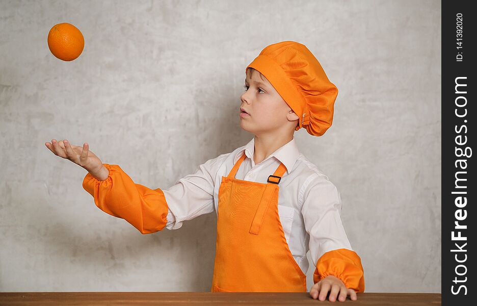 Cute boy in orange chef costume throws orange up