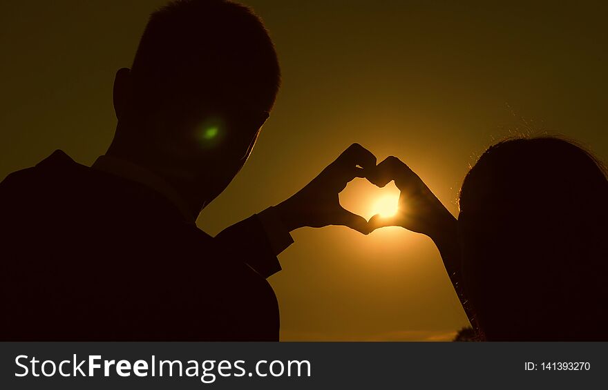 Sun is in the hands. A girl and her boyfriend making a heart shape by the hands opposite a beautiful sunset on the