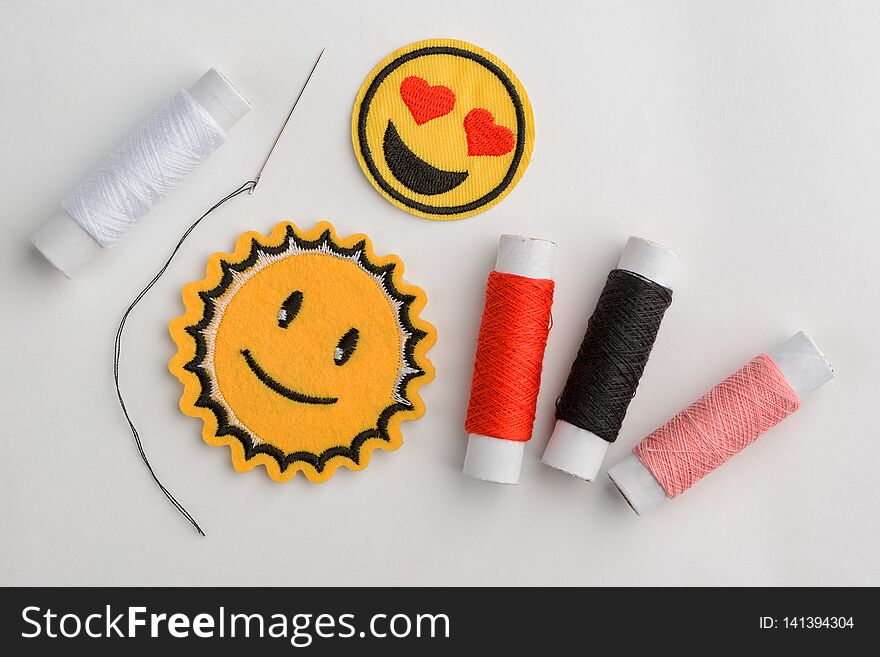 Emoji embroidered patches, needle and thread spools on white. Lovey-dovey eyes and smiling sun. Sewing, repair and clothes makeover. Emoji embroidered patches, needle and thread spools on white. Lovey-dovey eyes and smiling sun. Sewing, repair and clothes makeover.