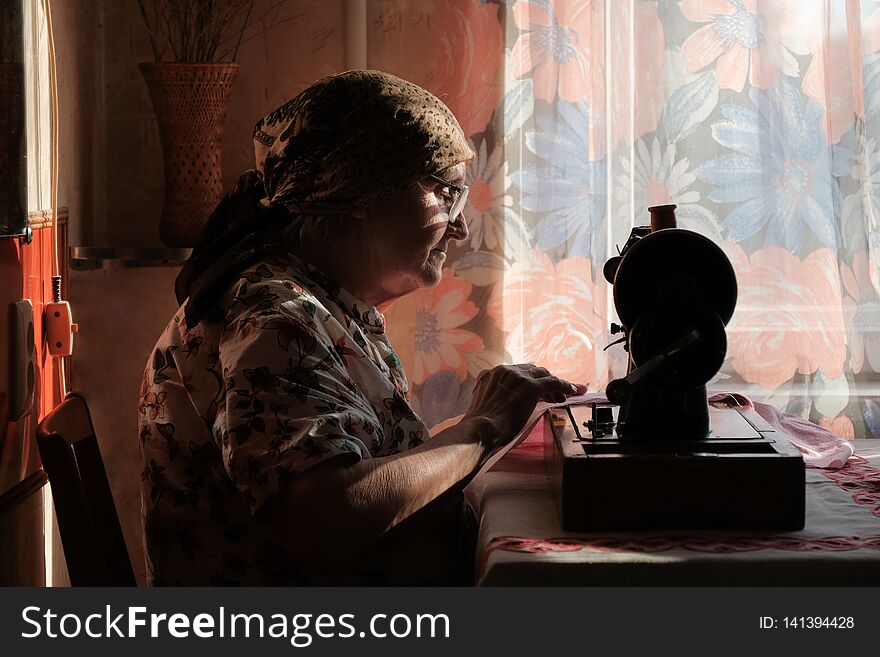 Senior woman in spectacles use sewing machine, silhouette of old dressmaker