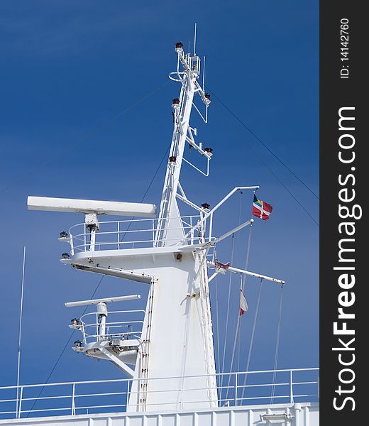 This is a close-up of ship mast with set of antennas against blue sky. This is a close-up of ship mast with set of antennas against blue sky