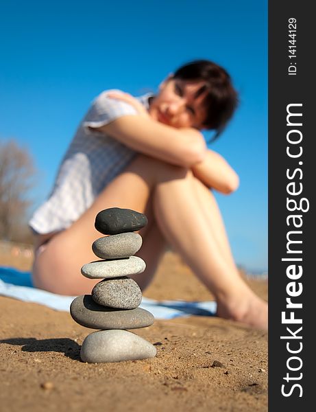 Young attractive woman sitting on the beach and looking at the stacked stones. Young attractive woman sitting on the beach and looking at the stacked stones
