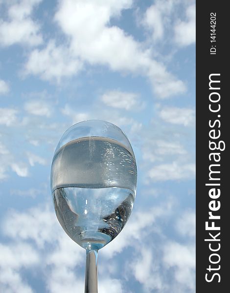 A glass of water against a bright cloudy blue sky background. A glass of water against a bright cloudy blue sky background