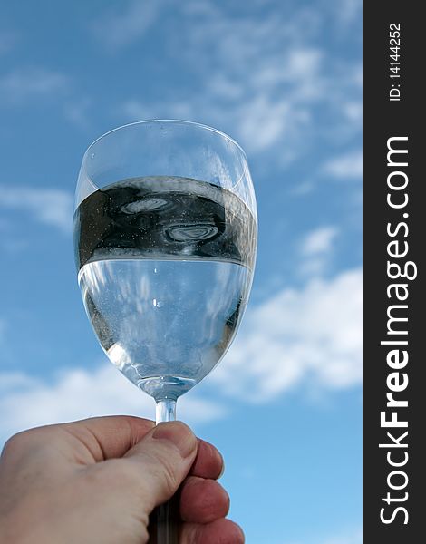 A glass of water held up in a toast against a bright cloudy blue sky background. A glass of water held up in a toast against a bright cloudy blue sky background