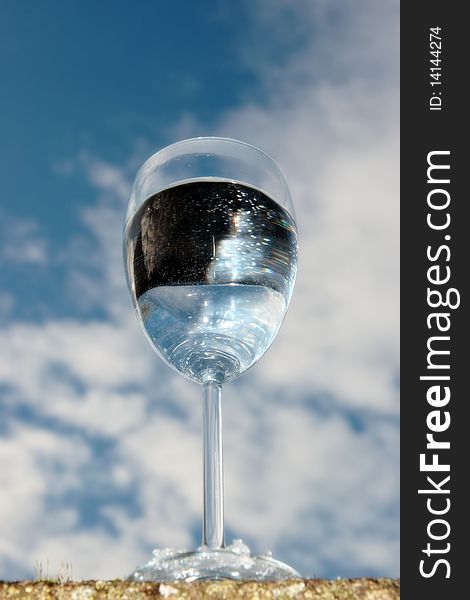 A glass of water on a wall against a bright cloudy blue sky background. A glass of water on a wall against a bright cloudy blue sky background