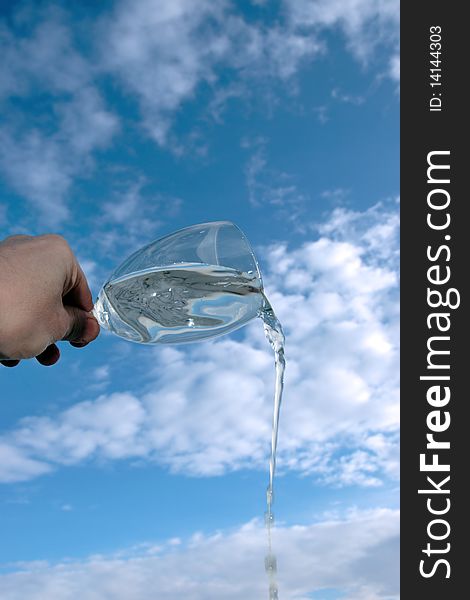 A glass of water being poured against a bright cloudy blue sky background. A glass of water being poured against a bright cloudy blue sky background