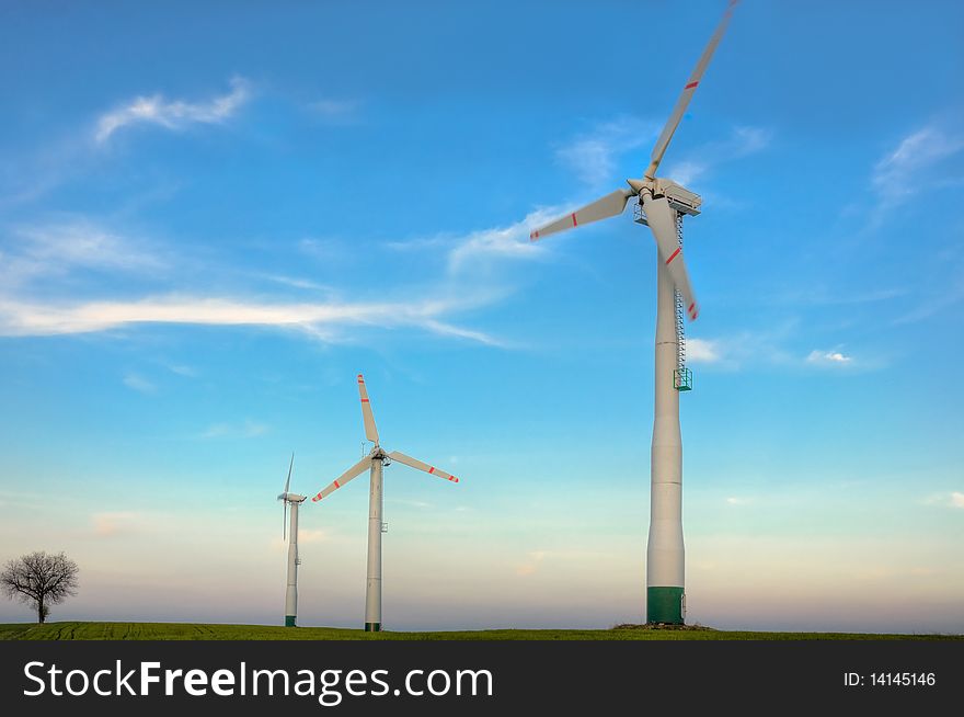 Three wind turbines and tree on blue sky with white clouds. Spring evening. Three wind turbines and tree on blue sky with white clouds. Spring evening.