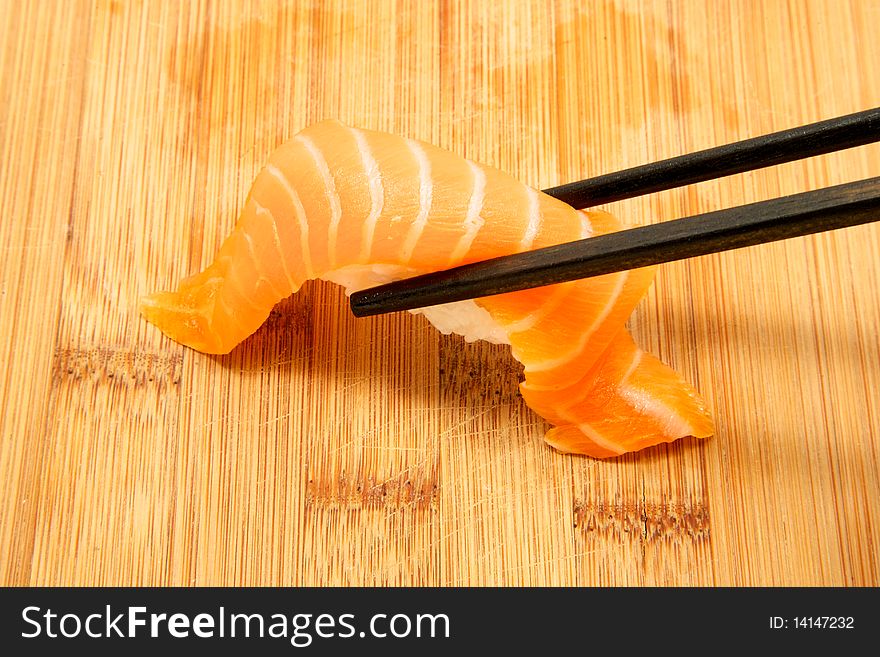 Close up of a piece of salmon nigiri being picked up with chop sticks. Close up of a piece of salmon nigiri being picked up with chop sticks