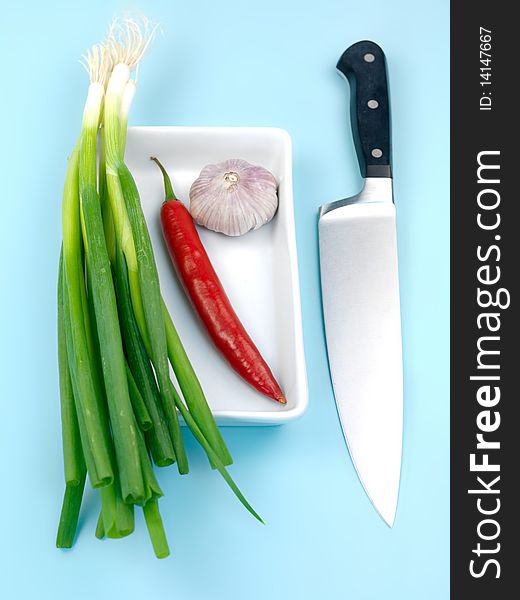 Spring onions, red pepper and garlic isolated against a blue background. Spring onions, red pepper and garlic isolated against a blue background