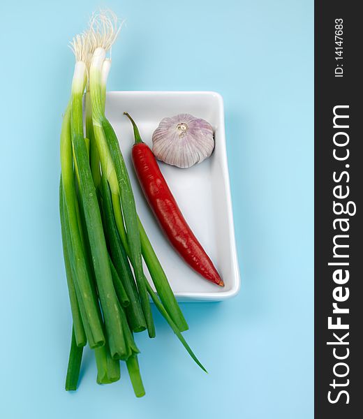 Spring onions, red pepper and garlic isolated against a blue background. Spring onions, red pepper and garlic isolated against a blue background