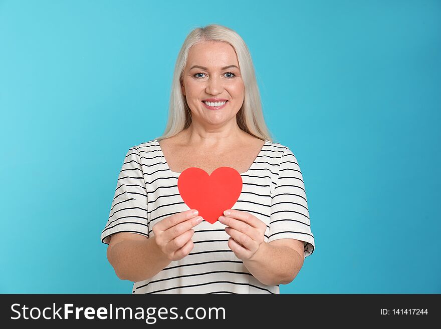 Portrait of mature woman with decorative paper heart on color background