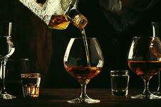 The Bartender Pours The Cognac Or Brandy In Big Wine Glass On The Old Bar Counter. Vintage Wooden Background In Pub Or Bar, Night Royalty Free Stock Photos