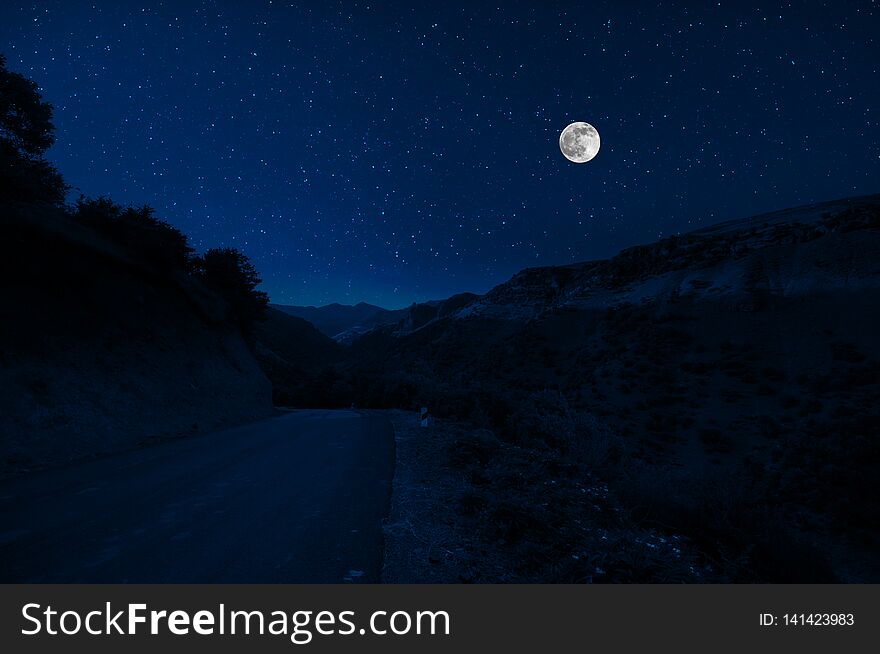 Mountain Road through the forest on a full moon night. Scenic night landscape of country road at night with large moon. Mountain Road through the forest on a full moon night. Scenic night landscape of country road at night with large moon