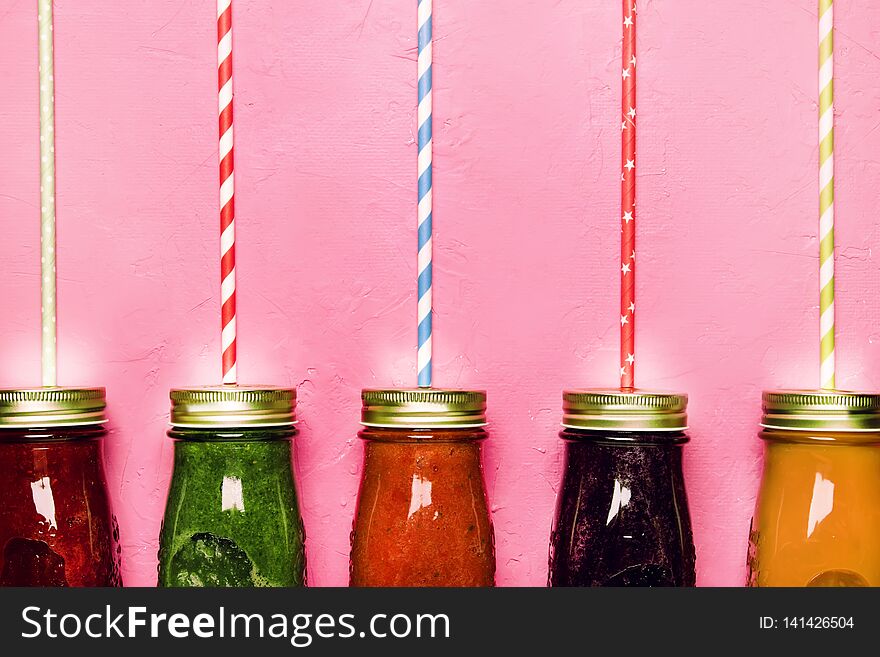 Multicolored detox vegan vegetable juices and smoothies in glass bottles on pink table, raw diet and clean food concept, drink background, copy space, top view