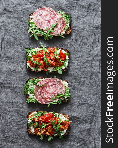 Tomatoes, italian sausage and rocket salad whole grain bread sandwiches on a gray background, top view. Copy space, flat lay. Delicious appetizers for wine, tapas