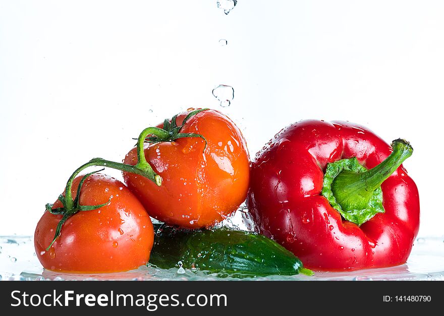 Fresh vegetables in a spray of water on a white background, tomato, cucumber, sweet pepper