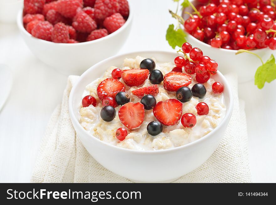 Tasty porridge with strawberry slices, black and red currants in bowl, close up