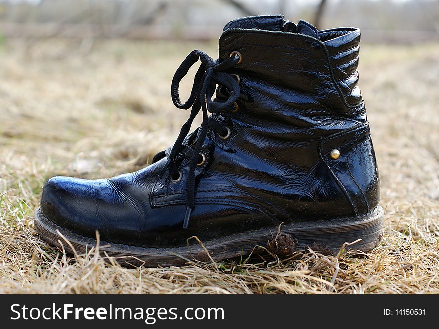 Dirty black boot on a dry grass background