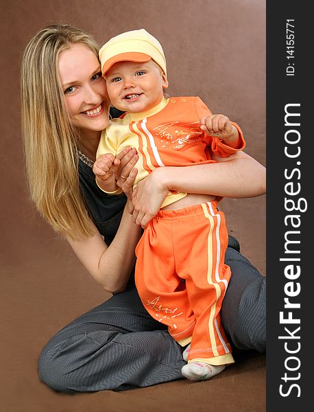 Young happy mother with baby in  orange suit on brown background