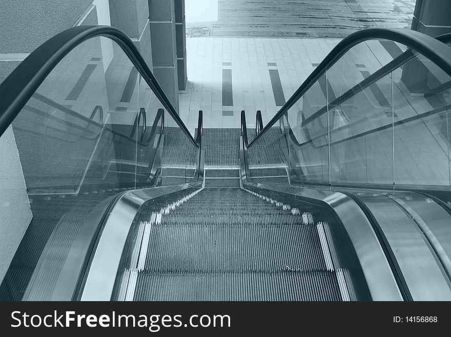 View of an escalator in an office building from above in blue tint. View of an escalator in an office building from above in blue tint